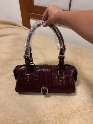 Vinröd guess croco-handväska med spänne - Snygg vinröd handväska i croco, från Guess. Köpt i Japan helt oanvänd