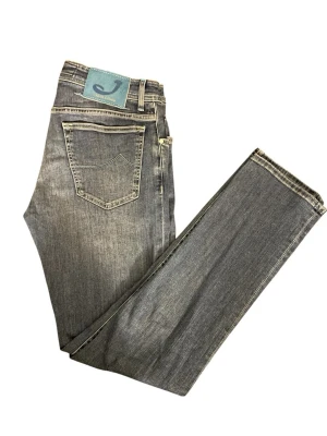 Blå jeans från Jacob Cohën - Snygga gråblå jeans från Jacob Cohën med klassisk femficksmodell och raka ben. Jeansen har en unik blå patch med logga bak i midjan och kontrastsömmar. Tillverkade i mjukt denimtyg som ger en avslappnad men stilren look.