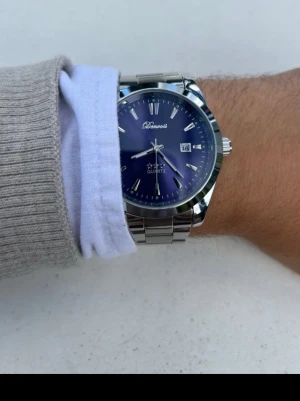 Silverfärgad Doventi klocka med blå urtavla - Stilren klocka från Doventi med blå urtavla och datumvisning. Klockan har ett klassiskt armband i silverfärgad metall och tydliga indexmarkeringar. Perfekt accessoar för dig som gillar en clean och modern look.