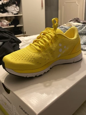 Gula löparskor från Craft - Snygga och sportiga löparskor från Craft i en riktigt fräsch gul färg med vita detaljer och svart sula. Ovandelen är i ventilerande meshmaterial och skon har klassisk snörning. Perfekta för dig som vill sticka ut på löprundan eller gymmet.