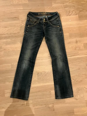 Mörkblå bootcut/straight  jeans från Guess - Snygga mörkblå bootcut jeans från Guess med slitningar och glittsömmar. Jeansen har dubbla knappar i midjan, fem fickor och dekorativa falska diamanter. En lätt tvättad look. 💕