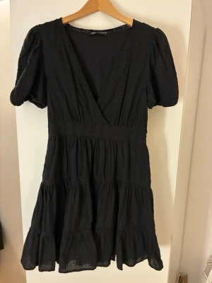 Svart kort klänning  - Svart klänning från Zara med v-ringning, puffärmar och volangdetaljer. Sträcker sig ner till knäna på mig (173)💕
