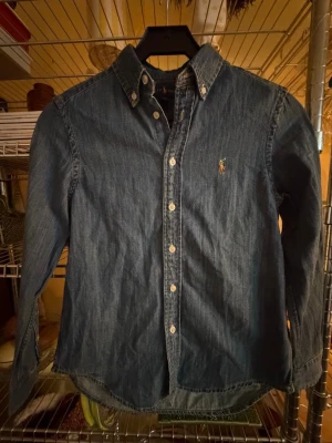 Blå jeansskjorta från Ralph Lauren - Klassisk blå jeansskjorta från Ralph Lauren. Perfekt för en stilren look. Storlek M för barn 10-12 år.  Pris kan diskuteras vid snabb affär!