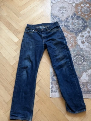 Levi's 751 raka blå jeans - Säljer ett par jeans från Levi's slitna i benslutet modell 751 i mörkblå denim. Jeansen har fem fickor, gylf med dragkedja och den ikoniska röda Levi's-lappen på bakfickan. Perfekta för en avslappnad och tidlös stil.