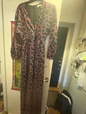 Persona by Malina cocktailklänning. Stl. S Ny, - Långklänning med svart bas och abstrakt rött och vitt mönster. Klänningen har v-ringning, långa ärmar med lätt puff och markerad midja. Tillverkad i ett glansigt, mjukt material som ger en elegant känsla. Perfekt för dig som vill sticka ut med en unik look. Skriv vid frågor. Med vänlig hälsning, Fanny 