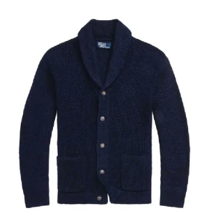 Mörkblå kabelstickad kofta Ralph Lauren - Koftan har en defekt det är att ena knappen på koftan är trasig men går fortfarande stänga, den är i två delar Snygg mörkblå kabelstickad kofta från Ralph Lauren med grov krage och silverfärgade knappar. Koftan har två framfickor och långärmad passform, perfekt för lager på lager. Materialet är mjukt och stickat, vilket ger en skön känsla och stilren look. Koftan är liten i storlek 