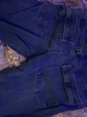 Blå bootcut jeans med bakfickor - Säljer ett par klassiska blå jeans med bootcut. De är lågmidjade och går att fixa till i midjan. Tillverkade i denim som ger en tidlös look och passar till många olika stilar.