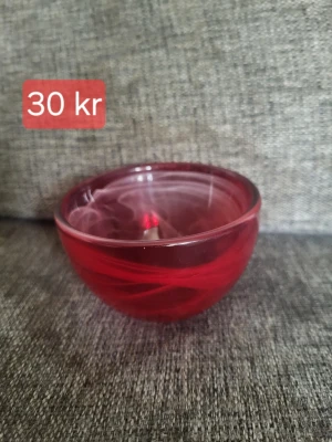 Röd glaskål med virvlande mönster - Säljer en rund skål i rött glas med snyggt virvlande mönster. Perfekt som dekoration eller för småprylar. Skålen har en blank yta och är genomskinlig med inslag av ljusare röda toner.