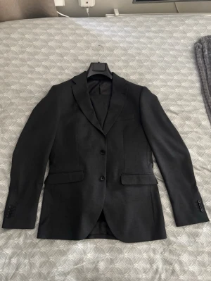 Mörkgrå riley kavajset - Säljer en mörkgrå kostymkavaj från riley med två knappar och klassiska slag. Kavajen har fickor med lock och är tillverkad i ett slätt material som ger en stilren look. Perfekt för dig som vill ha en tidlös och elegant outfit. Köpt för 5000kr hos brothers. Skriv vid frågor eller funderingar!