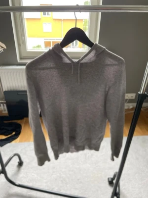 Grå cashmere hoodie från SayLess XS - Mjuk och stilren grå stickad hoodie från SayLess i 100% cashmere. Tröjan har huva med dragsko och ribbade muddar vid ärmslut och nederkant. Perfekt för dig som vill ha en enkel men lyxig look.