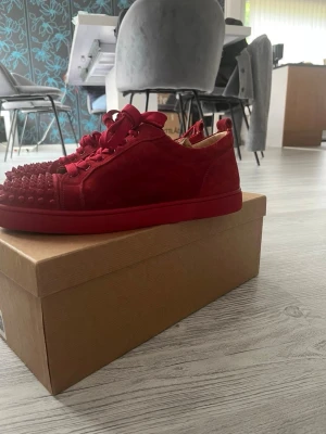 Röda  louboutin skor med spikar - Säljer ett par riktigt snygga röda sneakers i mocka med coola nitar på tån. Skorna har matchande röda skosnören och en chunky röd sula. Perfekta för dig som vill sticka ut och addera lite edge till din outfit.