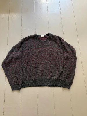 Pitti tröja  - Rundringad stickad tröja från danska Pitti. Melerad grå botten med geometriskt mönster i bordeaux/vinrött — den sortens grafiska jacquard-stickning som var typisk för 80-talets skandinaviska mode. Oversized och mjuk passform med ribbade muddar och krage. 90% akryl, 10% ull, tillverkad i Danmark.  Skick: Gott begagnat skick, inga anmärkningar. Märkt storlek XL men mer åt en M för boxig passform. Kontrollera alltid mått.  Mått:  Axelvidd: 70 cm Bröstvidd: 76 cm (152 cm) Längd: 70 cm Ärmlängd: 54
