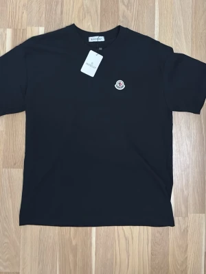 Svart Moncler t-shirt med logga - Svart moncler t-shirt storlek M helt oanvänd. Perfekt nu till sommaren. Skriv om du undrar något över tröjan. Priset kan diskuteras.