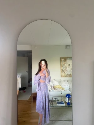 Adoore Ljuslila blommig omlottklänning - Supersöt ljuslila omlottklänning med blommigt mönster och knyt i midjan. Klänningen har v-ringning, volangdetaljer och vida trekvartsärmar. Perfekt för sommarens alla tillfällen!
