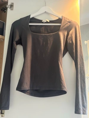 Grå långärmad topp med fyrkantig ringning - Stilren mörkgrå topp med lång ärm och fyrkantig ringning. Sitter snyggt och bekvämt. Perfekt att matcha med jeans eller kjol för en clean look.