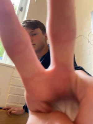Hand visar peace-tecken - En hand hålls upp framför kameran och visar ett tydligt peace-tecken med två fingrar. Bakgrunden visar en ljus vägg och ett fönster. Perfekt för dig som gillar symboliska gester eller vill ha en unik bild till dekoration.