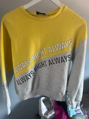 Gul och grå sweatshirt med text - Cool sweatshirt i färgblock med gul ovandel och grå nederdel. Tryckt text 'ALWAYS RIGHT ALWAYS' i vitt och svart snett över bröstet och magen. Rund halsringning och ribbade muddar. Perfekt för en avslappnad och trendig stil.