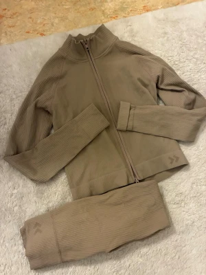 Beige ribbat träningsset 157 - Säljer ett beige ribbat träningsset från 157 med dragkedja på tröjan och matchande tights. Setet är tillverkat i stretchigt, perfekt för gymmet. Använt plagget 2 gånger✨