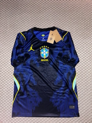  Brasilien fotbollströja - Snygg blå fotbollströja från Brasilien med gula detaljer och CBF-emblem på bröstet. Tröjan har korta ärmar, sportig passform och är tillverkad i ett lätt, ventilerande material. Perfekt för fotbollsträning eller att bära som supporter.
