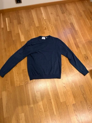 Mörkblå rundhalsad tröja - En enkel och stilren mörkblå tröja med rund halsringning och långa ärmar. Tröjan är tillverkad i ett tunt, mjukt material som passar perfekt för lager på lager. Ribbstickade muddar vid ärmslut och nederkant ger en klassisk look.