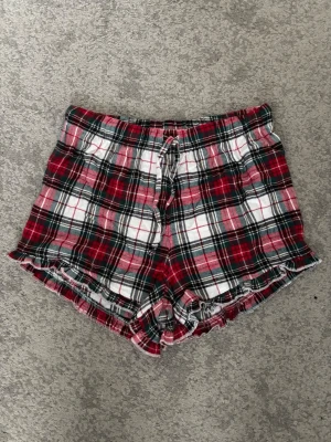 Rutiga pyjamasshorts med volangkant - Mysiga pyjamasshorts med röd, vit och svart rutigt mönster. Shorts med elastisk midja och knytband samt volangkant längst ner. Perfekta för chillkvällar hemma.