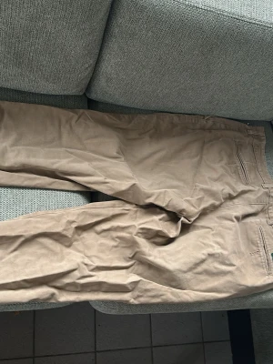 Beige chinos med raka ben - Säljer ett par klassiska beige chinos med raka ben och diskreta bakfickor. Byxorna har en enkel design och är tillverkade i ett mjukt bomullsmaterial som känns skönt mot huden. Perfekta för en avslappnad och stilren look. Ingen knapp