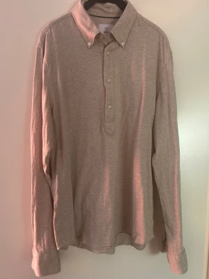 Beige tröja med knappar - Klassisk beige tröja från bläck med lång ärm och knappar framtill. Skjortan har en mjuk bomullskänsla och button-down krage, perfekt för en avslappnad men ändå stilren look. Några sömmar har gått upp på baksidan (se sista bild) men inget hål eller något som påverkar.