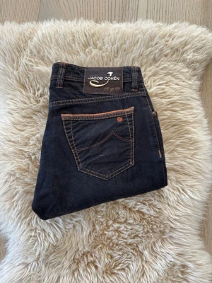 Jacob Cohen ltd - Snygga mörkblå jeans från Jacob Cohen med kontrastsömmar i beige och coola detaljer som broderad logga på fickan. Klassisk femficksmodell i mjukt denimtyg som passar perfekt till en avslappnad men stilren look.