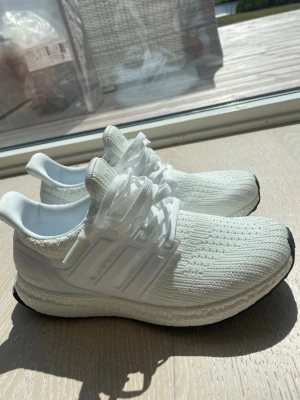 Vita Adidas Ultraboost sneakers - 🇨🇳🇨🇳Fräscha vita Adidas Ultraboost sneakers med stickad ovandel och klassiska tre ränder på sidan. Skorna har en chunky sula med Boost-dämpning och svart yttersula. Perfekta för dig som gillar sportig och clean stil. 🇨🇳🇨🇳