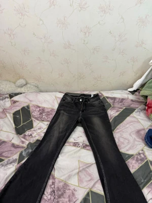 Svarta bootcut jeans med vita sömmar - Säljer ett par svarta bootcut jeans med markerade vita sömmar och slitningar framtill. Jeansen har klassisk femficksmodell och låg midja. Perfekta för dig som gillar en retro och avslappnad stil. Passar också för tjejer som är under 155