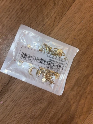 Nageldekorationer mix guld och rosa - Säljer ett set med nageldekorationer, inklusive guldiga metallfigurer som stjärnor, månar och solar samt en ask med små dekorationsbitar (blommor) i rosa, vitt och guld. Perfekt för att skapa unika och kreativa nageldesigner.