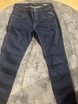Mörkblå jeans Replay Anbass - Snygga mörkblå jeans från Replay, modell Anbass. Klassisk femficksdesign med kontrastsömmar och raka ben. Jeansen är tillverkade i denim med en skön stretch som gör dem bekväma att bära. Perfekt för dig som gillar stilrena och moderna jeans.