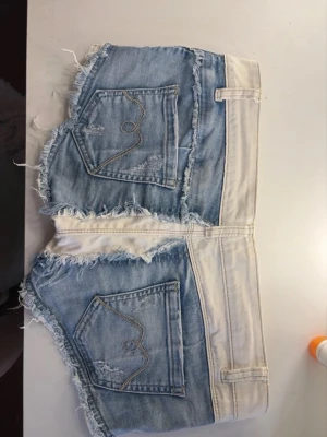 Sjukt snygga shorts - Unika shorts från Yves Jeans Couture i vit och ljusblå denim med råa fransar och slitna detaljer. Shortsens design har kontrasterande paneler och snygga bakfickor med broderi. Perfekt för dig som vill sticka ut i sommar!