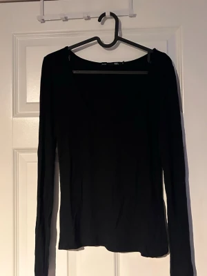 Svart långärmad topp  - En enkel och stilren svart långärmad topp från Gina Tricot. Toppen har en djupare rundringning och är i ett mjukt, stretchigt material som sitter snyggt på kroppen. Perfekt att matcha med jeans eller kjol.