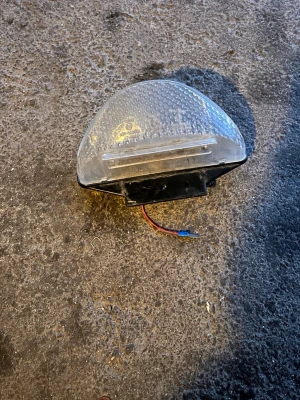 Halvrund belysningsarmatur plast - Säljer en halvrund belysningsarmatur i genomskinlig plast med svart baksida och monteringsskruvar. Lampan har anslutningskablar i rött och gult, och är tänkt för vägg- eller takmontering. Perfekt för garage, förråd eller liknande utrymmen.