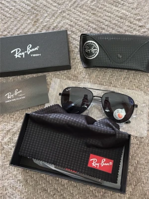 Rayban solglasögon  - Snygga svarta Ray-Ban Tech solglasögon med klassisk pilotform och mörka glas. Bågarna är tillverkade i lätt syntetmaterial från Carbon Fiber Collection. Kommer med originalfodral, putsduk och box. Perfekta för dig som vill ha en clean och tidlös look.