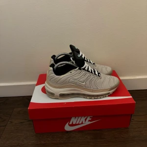 Nike Air Max Plus vita sneakers - Nike Air Max Plus sneakers i vitt och beige med svarta detaljer och turkos logga på plösen. Skorna har en vågig design på ovandelen, vita snören och synlig Air Max-sula. Perfekta för dig som gillar streetwear och sportig stil. Lite småslit här och där men skorna funkar fortfarande mycket bra 
