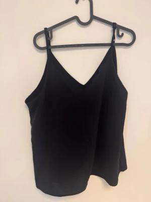 Svart scallop linne - Linne med v-ringning med vågigt/scallop skärning i strl XL. Oklart märke. Ställbara axelband. Silkigt och något transparent material.   Sparsamt använt och i gott skick. Hittar ingenting att anmärka på.