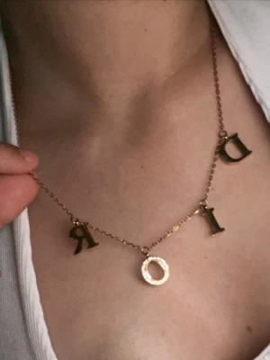 Guldhalsband bokstäver - Snyggt halsband i guld  med hängande bokstäver som stavar D I O R. O:et är dekorerat med små vita pärlor för extra bling. Perfekt statement-piece för dig som gillar lyxiga accessoarer och vill sticka ut.