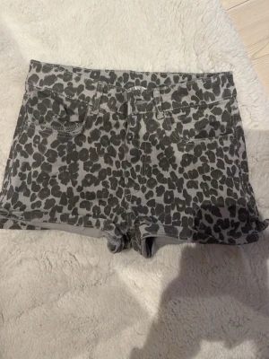 Grå leopardmönstrade jeansshorts - Snygga grå jeansshorts med svart leopardmönster. Klassisk femficksmodell med bälteshällor och korta ben. Perfekta för dig som vill sticka ut med ett djurmönster i garderoben. Materialet känns som stretchig denim för extra komfort. Shortsen är i helt jätte bra skick!🤗