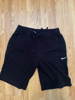 Svarta Nike shorts med snörning mycket bra skick - Svarta shorts från Nike med klassisk vit logga på benet. Modellen har elastisk midja med snörning för skön passform och sidofickor. Perfekta för träning eller chill dagar. Materialet känns mjukt och lätt, troligen bomull eller bomullsblandning. Storlek M men passform är S.