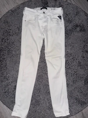 Vita skinny jeans från replay - Säljer ett par vita skinny jeans från replay med klassisk femficksdesign och läderpatch bak i midjan. Jeansen har smal passform och är tillverkade i ett stretchigt bomullsmaterial för extra komfort. Perfekta för en clean och fräsch look.