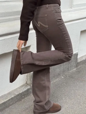 Nelly, Bruna bootcut jeans med kontrastsöm - Snygga bruna bootcut jeans med kontrastsömmar och klassisk femficksdesign. Jeansen har hög midja, utsvängda ben och dubbla knappar i midjan. Perfekta för en trendig och avslappnad look. Helt oanvända! Nypris: 699kr 