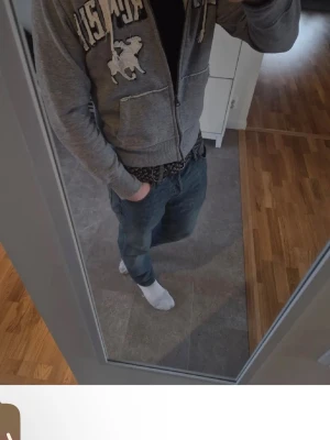 Grå hoodie från Abercrombie & Fitch - Snygg grå zip-hoodie från Abercrombie & Fitch med vit logga och broderad älg på bröstet. Mjuk insida, dragsko i huvan och två fickor framtill. Perfekt för en avslappnad och cool stil.