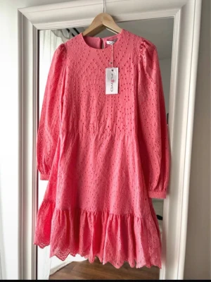 Rosa sommar klänning från Floyd - Supersöt korallrosa klänning från Floyd i modellen Miella. Klänningen har lång ärm, rund halsringning och fina broderade detaljer över hela tyget. Kjolen har volangkant och klänningen är i en kort modell. Perfekt för dig som gillar färg och detaljer! 100% bomull, Originalpris 999kr. 