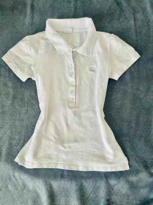 Vit kortärmad pikéskjorta - Klassisk vit pikéskjorta med krage och knappar framtill. Skjortan har korta ärmar och är figursydd för en snygg passform. Perfekt för en clean och stilren look.
