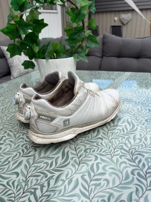 FOOTJOY PRO/SL BOA golfskor strl 42 - Säljer ett par vita FootJoy Pro SL golfskor med BOA-snörning för enkel justering. Skorna har slitstark ovandel i syntetmaterial och greppsäker yttersula med blå och grå detaljer. Perfekta för dig som vill ha stabilitet och komfort på golfbanan.
