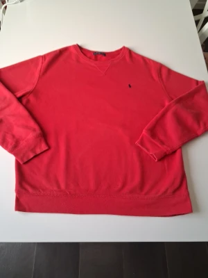 Röd crewneck från Ralph Lauren - Röd långärmad crewneck från Ralph Lauren med klassisk broderad logga på bröstet. Tröjan har rund halsringning och ribbade muddar vid ärmslut och nederkant. Perfekt för en chill och stilren look. Varan är i mycket bra skick i storlek S. Hör av dig vid frågor