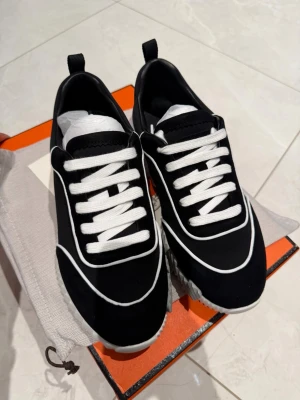 Svarta sneakers från … - Stilrena svarta sneakers från .. med vita kontrasterande detaljer och vita skosnören. Skorna har en låg silhuett och en räfflad vit sula som ger en modern touch. Materialet ser ut att vara mocka och textil, vilket ger en lyxig känsla.