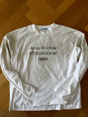 Vit långärmad Acne Studios t-shirt - Säljer en vit långärmad t-shirt från Acne Studios med tryck på bröstet där det står 'Acne Studios STOCKHOLM 1996'. Klassisk rund hals och relaxed fit. Tillverkad i bomull och true hemp som känns skön mot huden. Köpt i butik